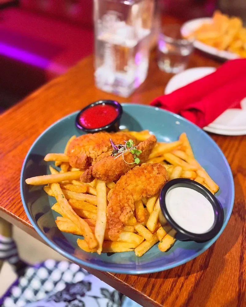 A blue plate of crispy chicken tenders and french fries with two dipping sauces.