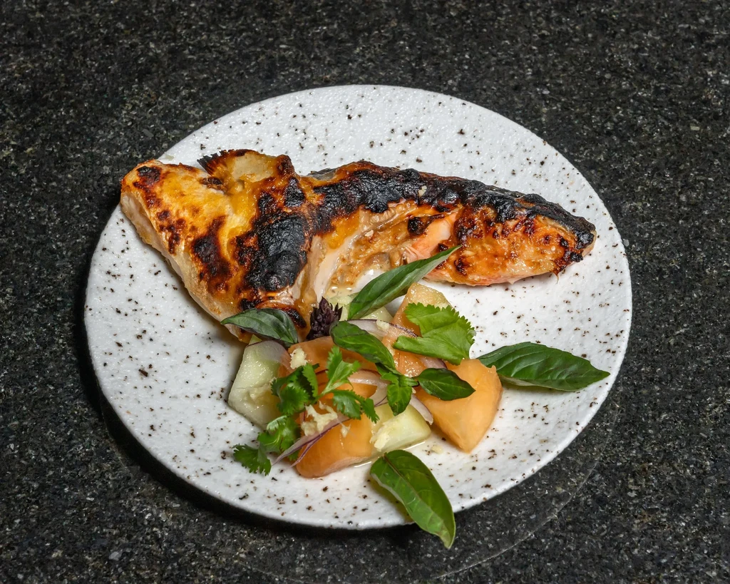 Grilled salmon fillet with melon and cucumber salad on a white plate.