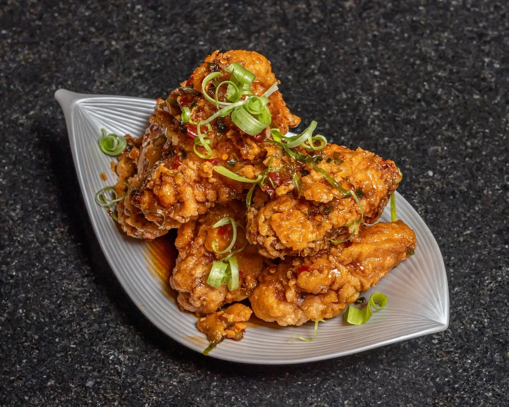 Fried chicken wings with sauce and green onions on a gray plate.