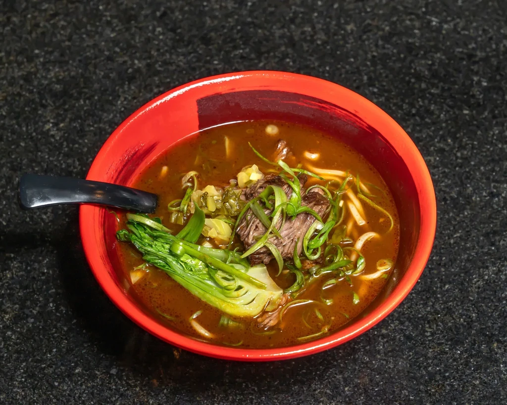 A bowl of beef ramen with bok choy, green onions, and noodles.