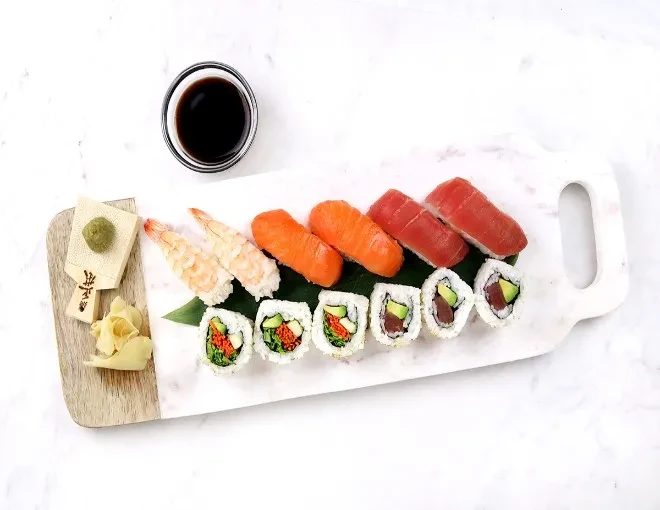 Assorted sushi, rolls, wasabi, ginger, and soy sauce on a white board.