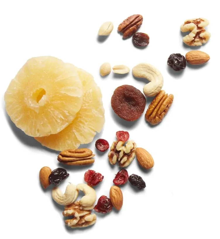 Dried pineapple rings, assorted nuts, and dried fruit on white surface.