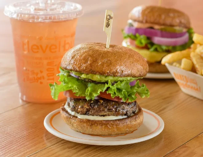 Two burgers, fries, and a drink on a wooden table.