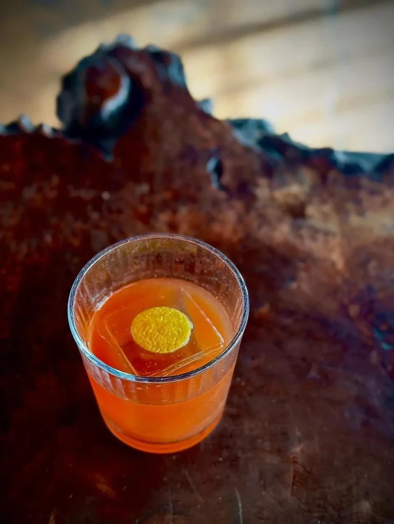 A cocktail with a round yellow garnish and ice on a wooden table.