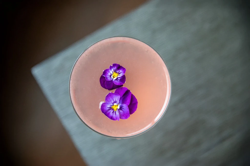 Overhead view of a pink cocktail garnished with two purple pansies.
