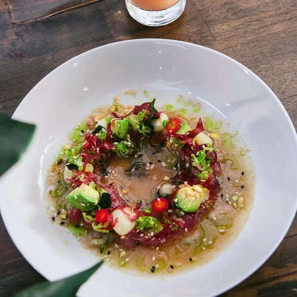 A white bowl of tuna tartare with avocado, herbs, and sauce.