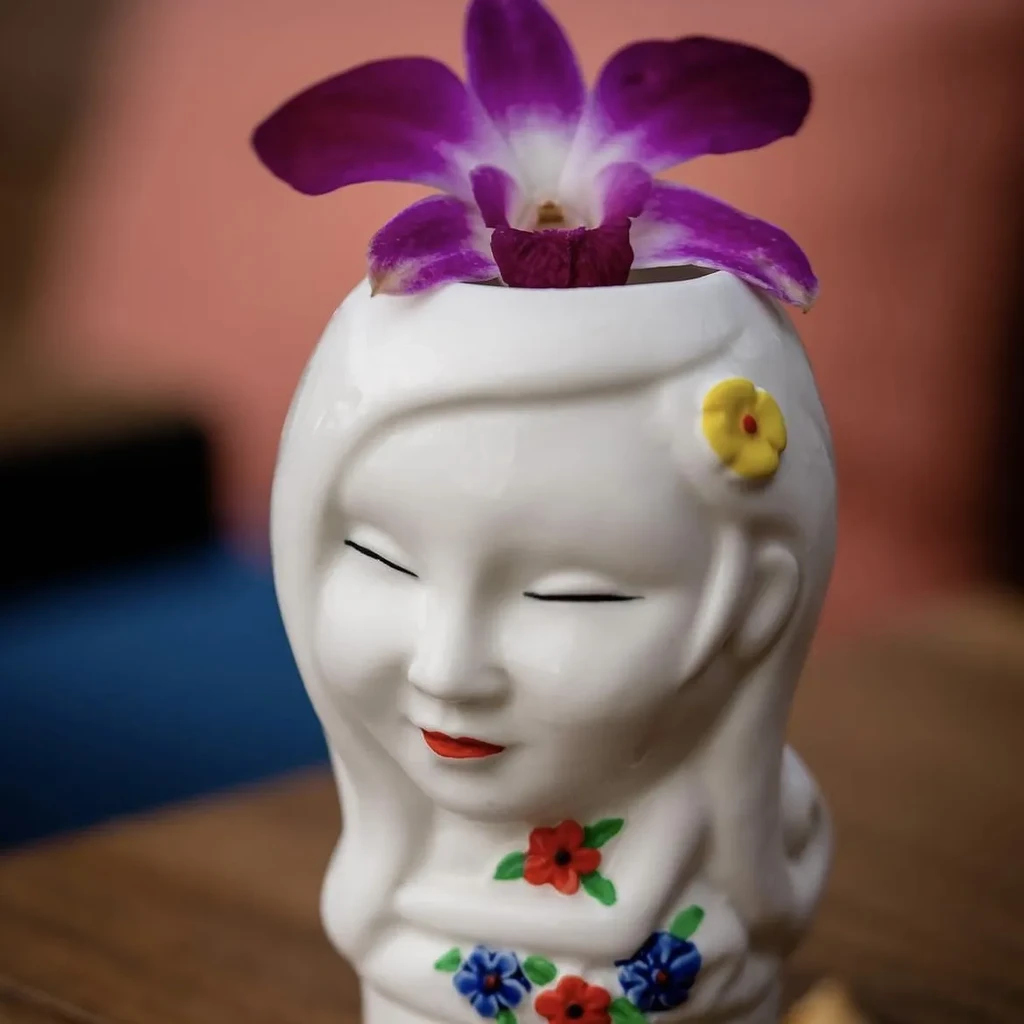 White ceramic vase shaped like a girl's head with a purple orchid.