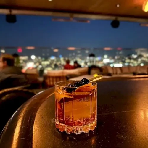 Cocktail with orange and berries on a rooftop bar at dusk.