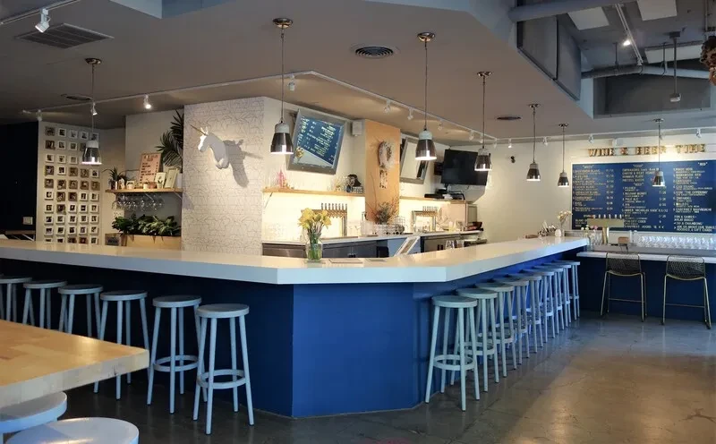 Empty bar with white stools, blue counter, and "Wine & Beer Time" sign.