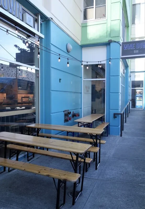 Outdoor patio with wooden picnic tables and string lights outside a blue building.