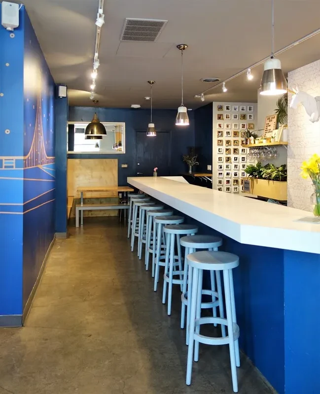 Long white bar with light blue stools in a blue-walled restaurant.