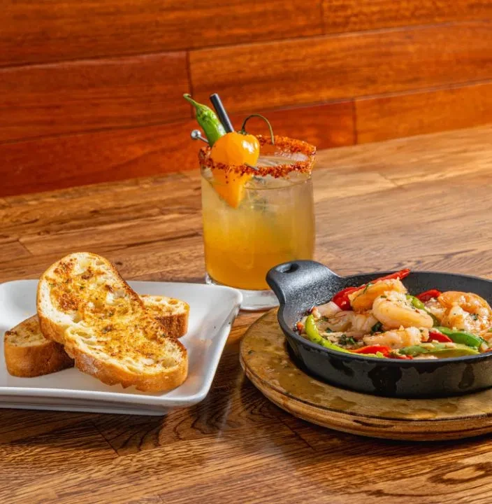 Shrimp skillet with garlic toast and a pepper-garnished cocktail.