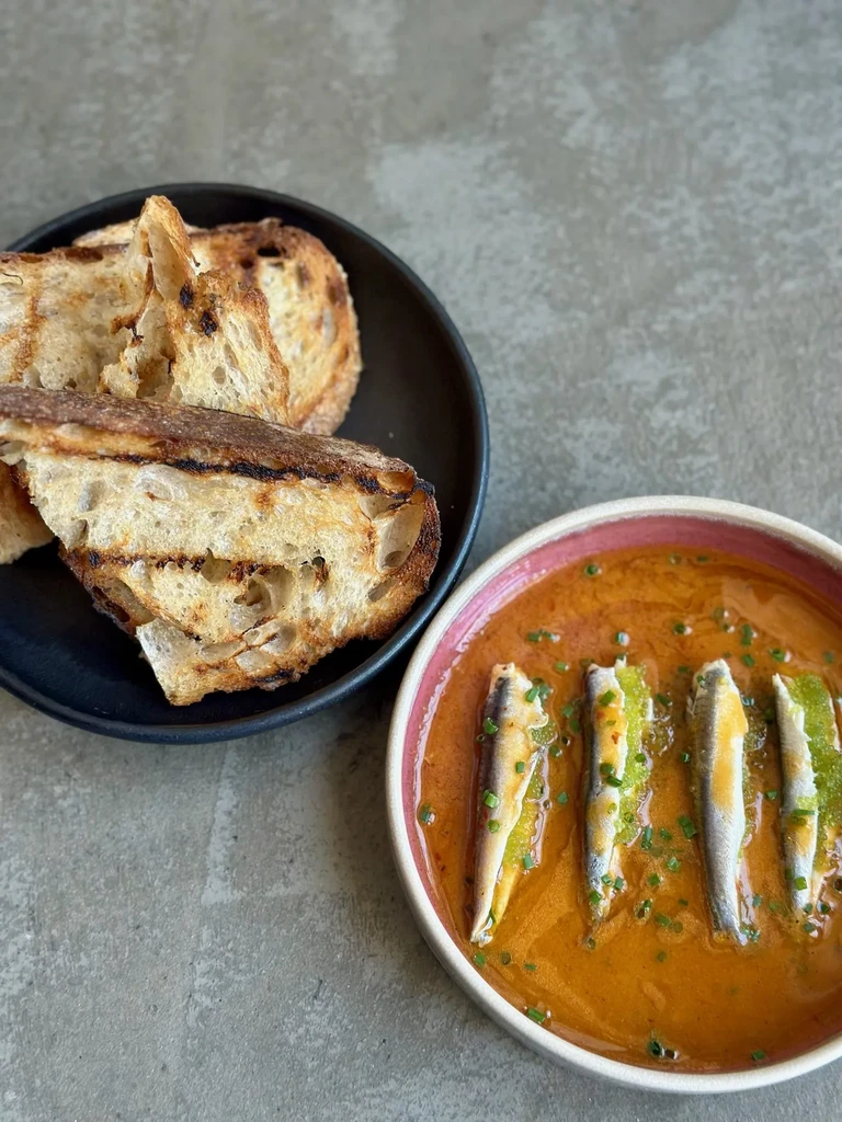 A bowl of four whole sardines in sauce with a side of toasted bread.