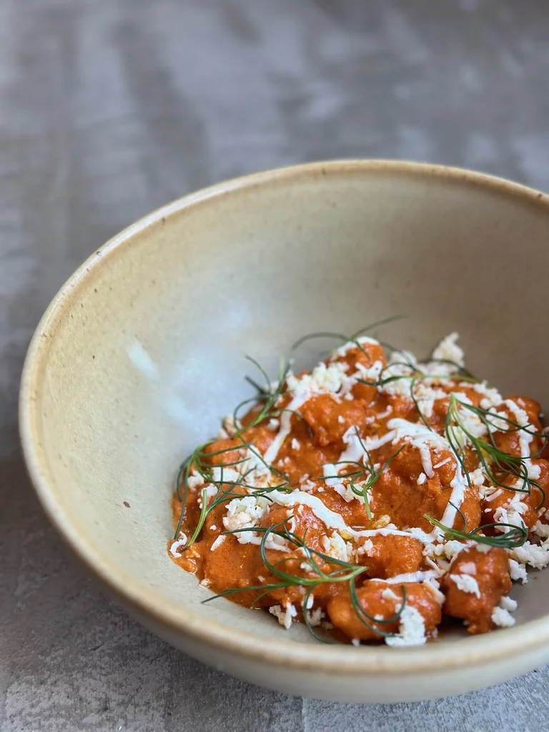 A beige bowl filled with orange gnocchi, white cheese, and dill sprigs.