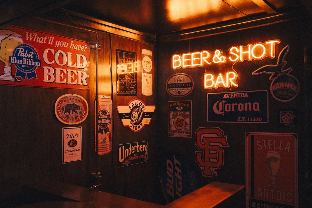 Bar wall covered with beer and liquor signs, illuminated by neon light.