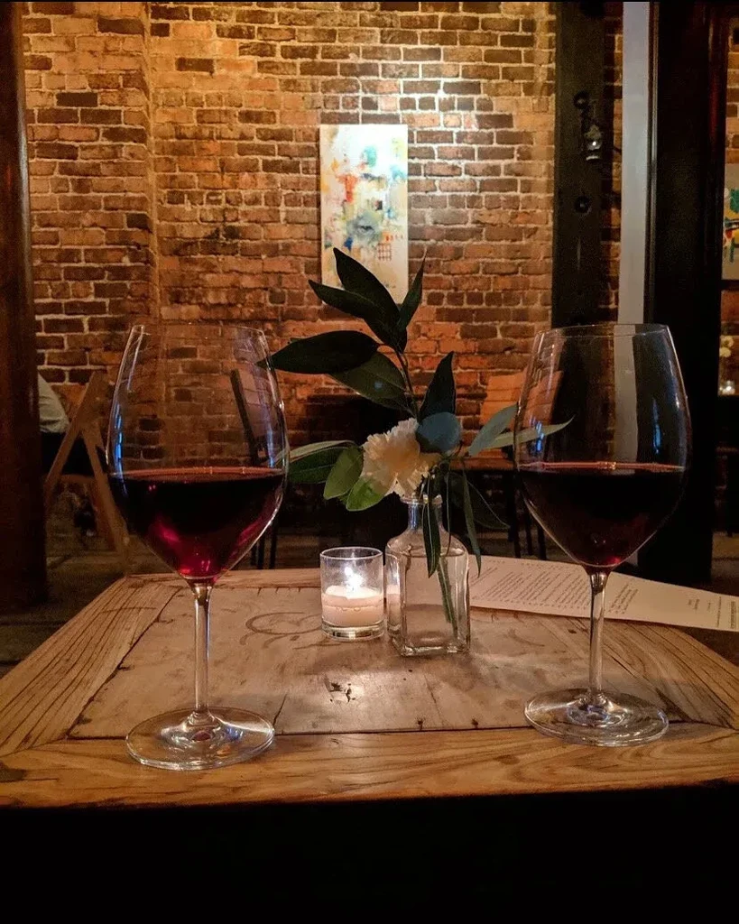 Two glasses of red wine on a table with a brick wall background.