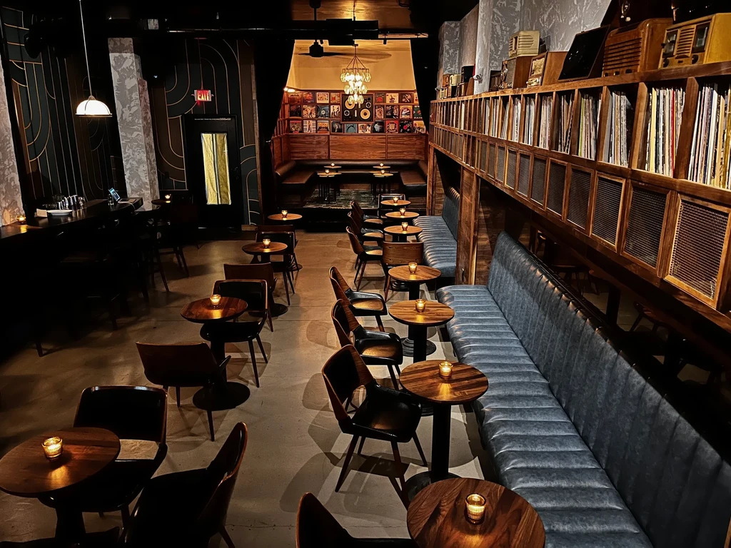 Dark, empty bar with long booth seating and vinyl record shelves.