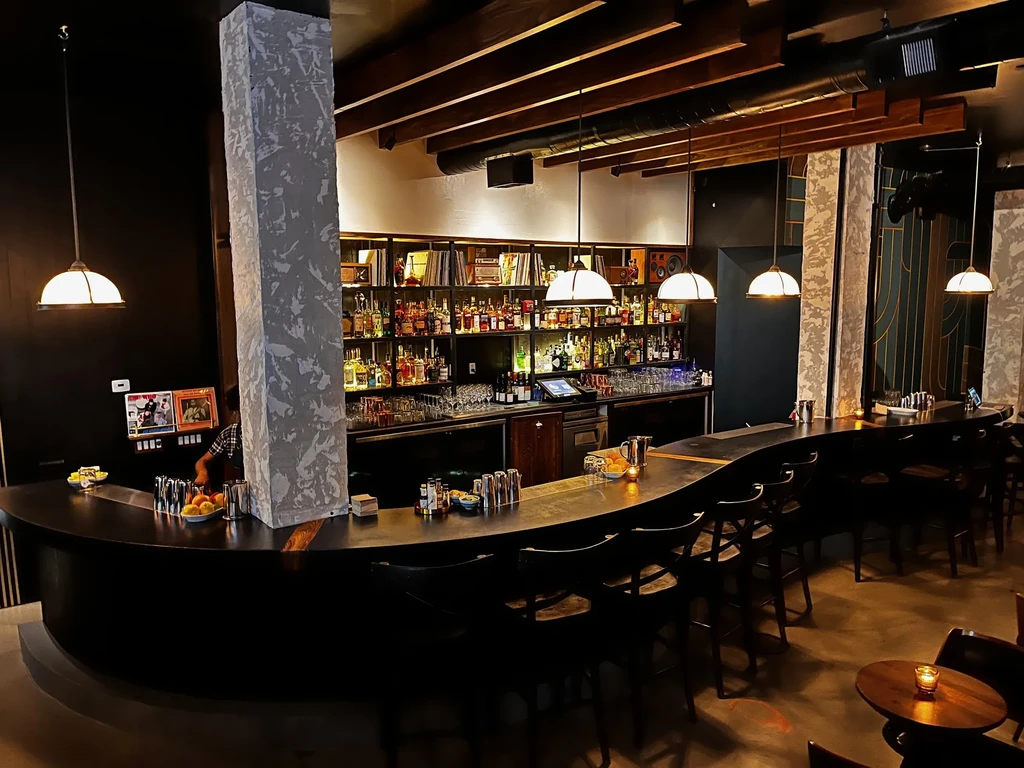 A dimly lit, stylish cocktail lounge with a long dark bar.