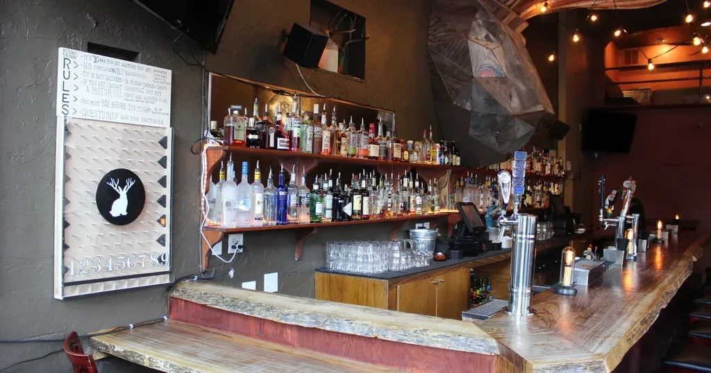 Interior view of a dimly lit bar with numerous bottles and a wooden countertop.