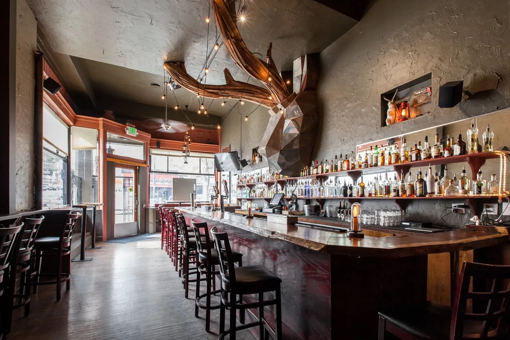 A rustic bar with a geometric deer head sculpture and extensive liquor collection.