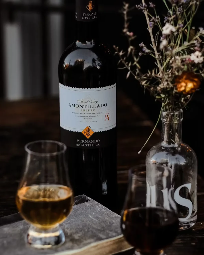 A bottle of sherry, two glasses of alcohol, and a flower vase.