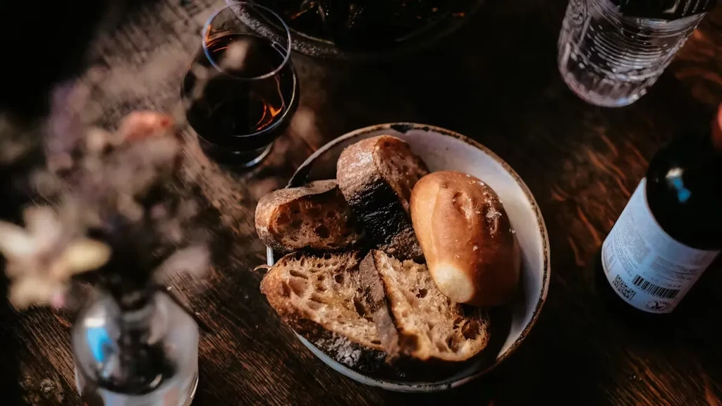 A bowl of bread, a glass of red wine, and a bottle.