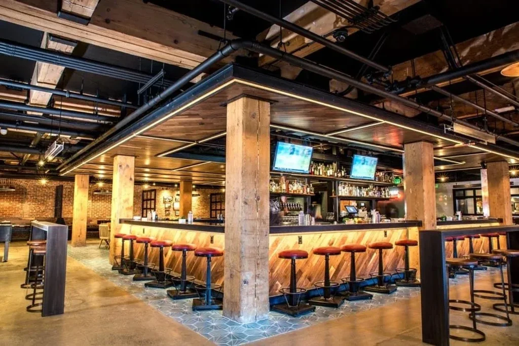 A long bar with red stools, wood panels, and exposed pipes overhead.