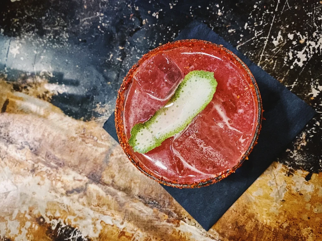 Overhead shot of a red cocktail with a lime peel garnish.