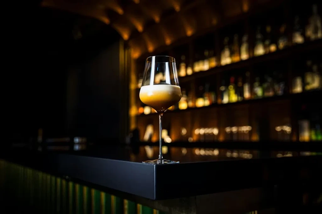 A cocktail in a wine glass on a dark bar counter.