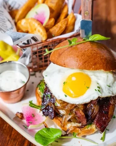 A burger with a fried egg, bacon, caramelized onions, and potato wedges.