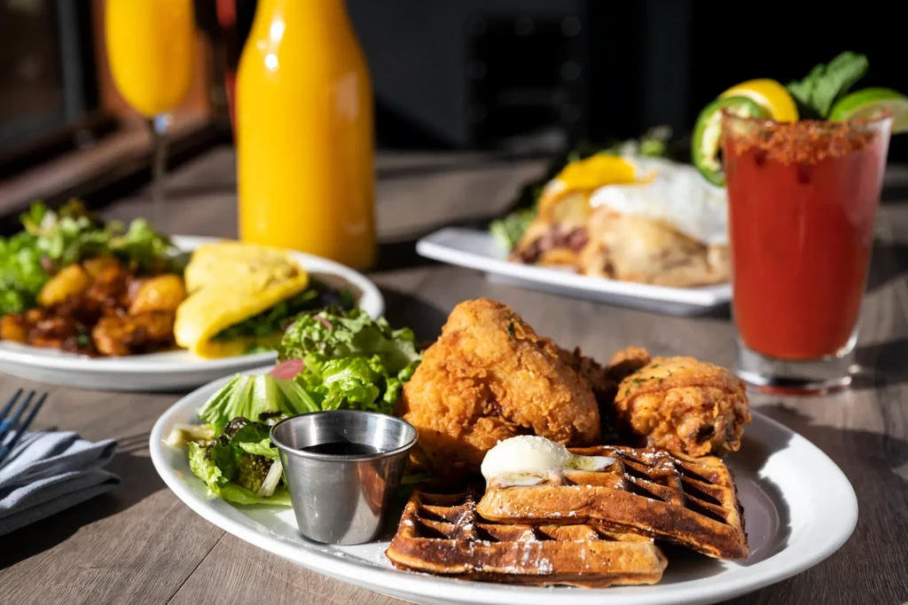 Plates of breakfast items, including chicken and waffles, with drinks on a table.