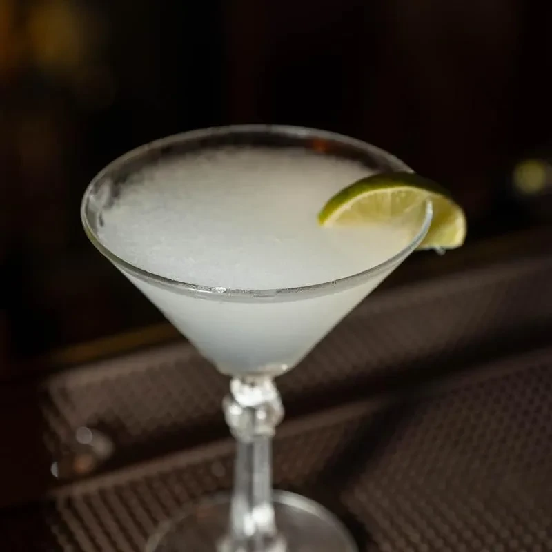 A frozen margarita or daiquiri in a martini glass with a lime wedge.