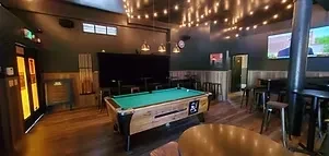 A pool table is in the center of a warmly lit bar.