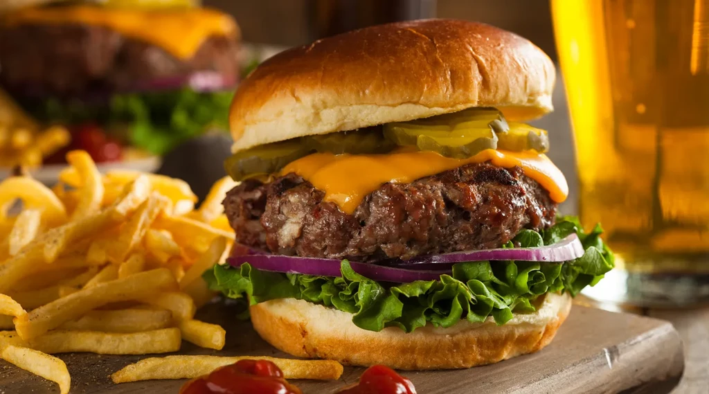Cheeseburger, fries, and a beer on a wooden board.