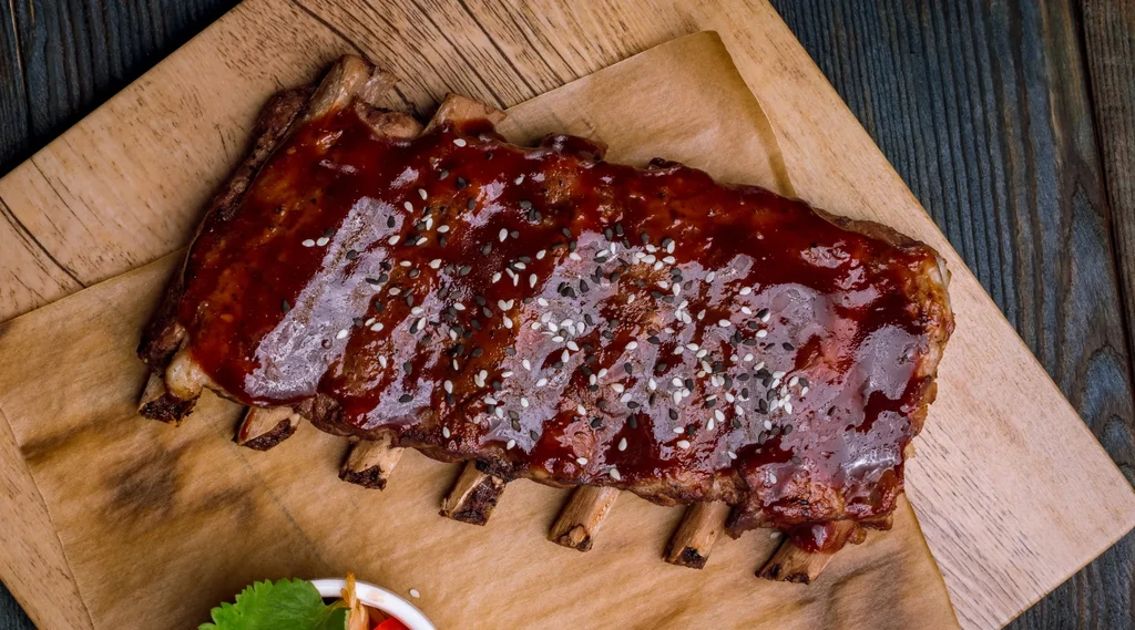 Rack of ribs with barbecue sauce and sesame seeds on a board.