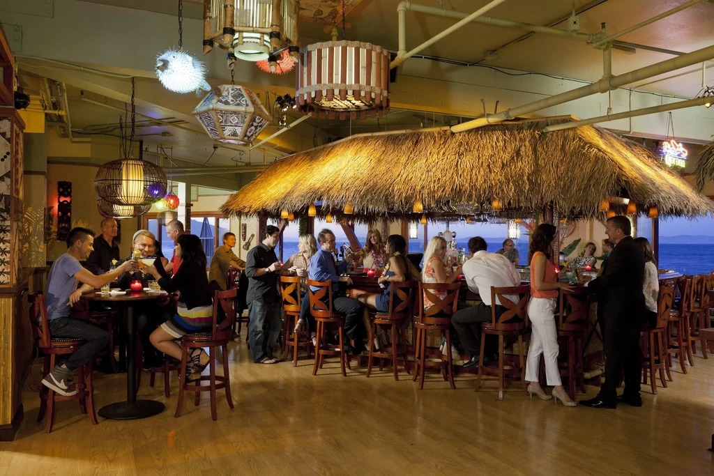 People socialize at a tiki bar by the ocean at sunset.