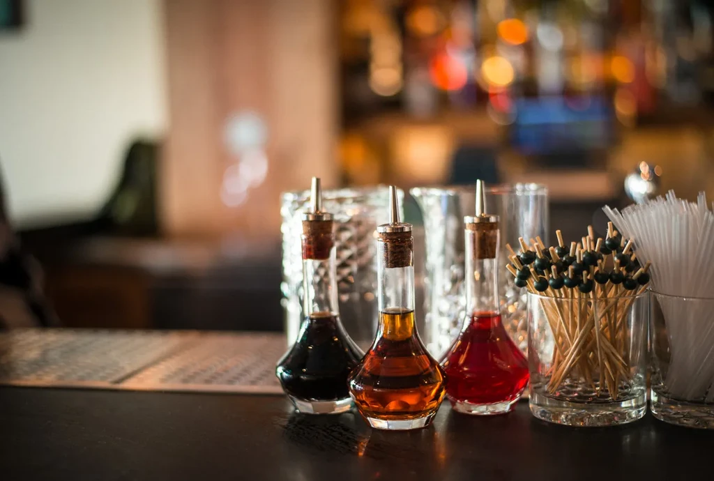 Three bitters bottles, cocktail picks, and straws on a bar.