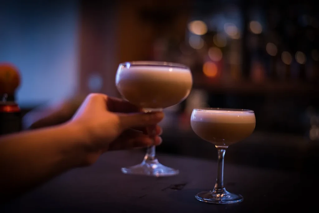A person's hand picks up a cocktail with foam from a bar.