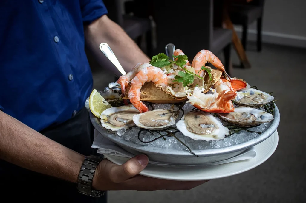 A person serves a platter of shrimp, crab, and oysters on ice.