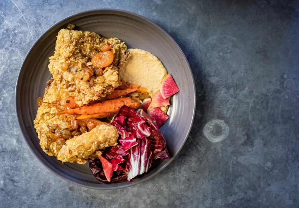 A plate of fried chicken, carrots, and salad on a dark gray surface.