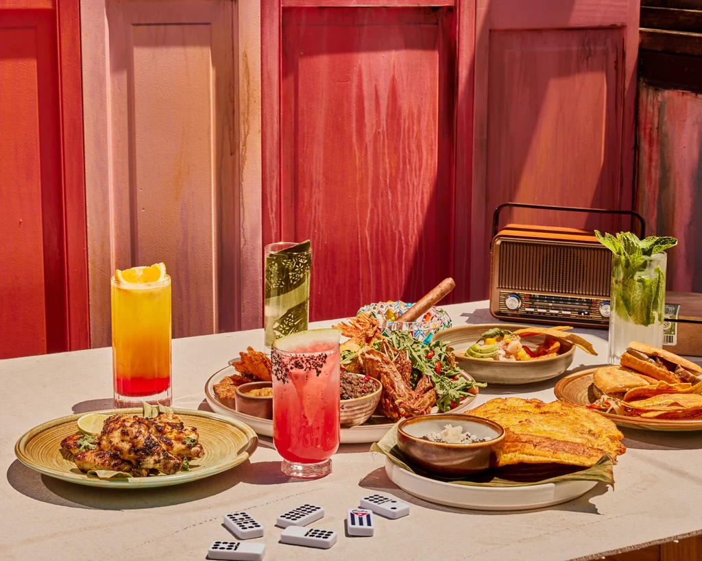 Table laden with Cuban food, drinks, dominoes, and a vintage radio.