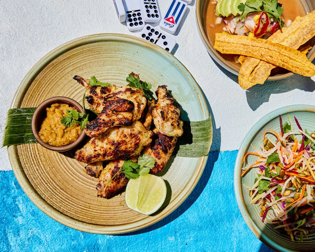 Grilled chicken with sides, dominoes, and ceviche on a blue and white table.