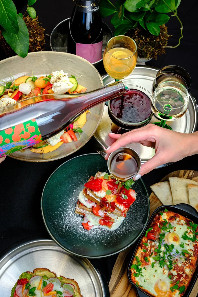 Overhead shot of a table with several dishes, drinks, and a hand pouring syrup.