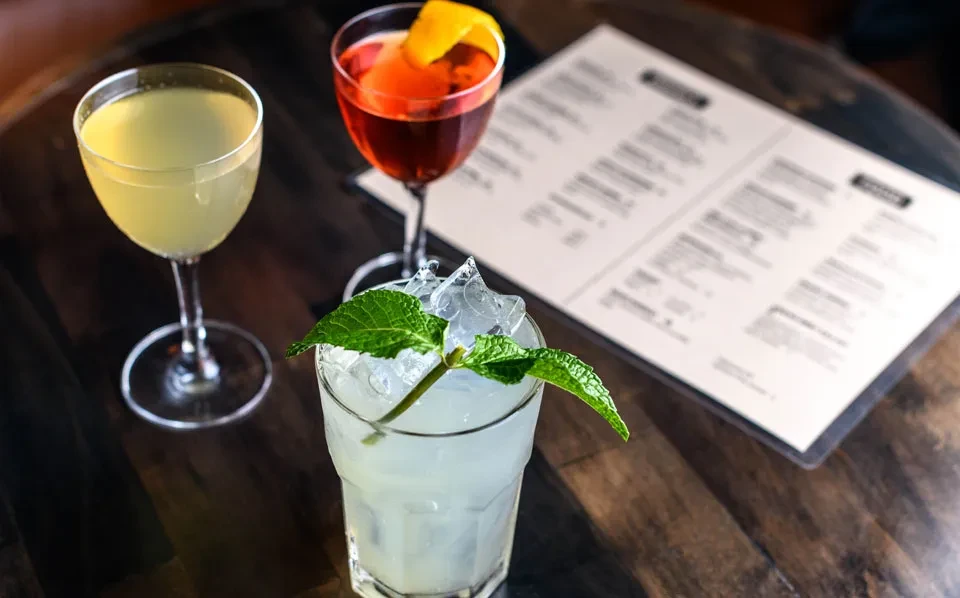 Three cocktails and a menu on a dark wood table.