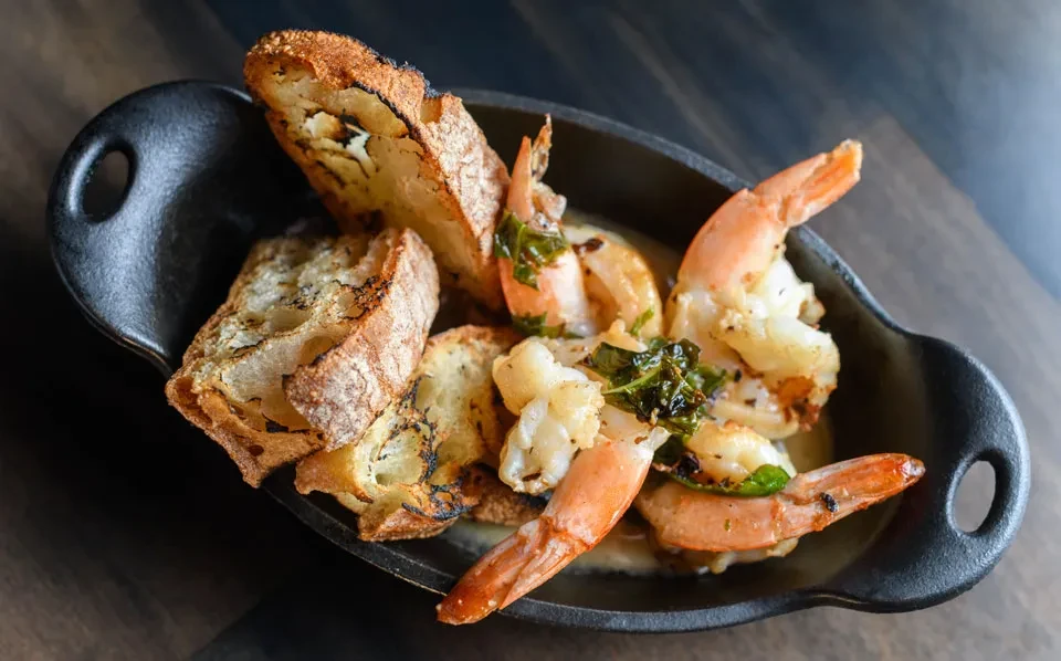 Shrimp scampi in a black skillet with toasted bread slices.