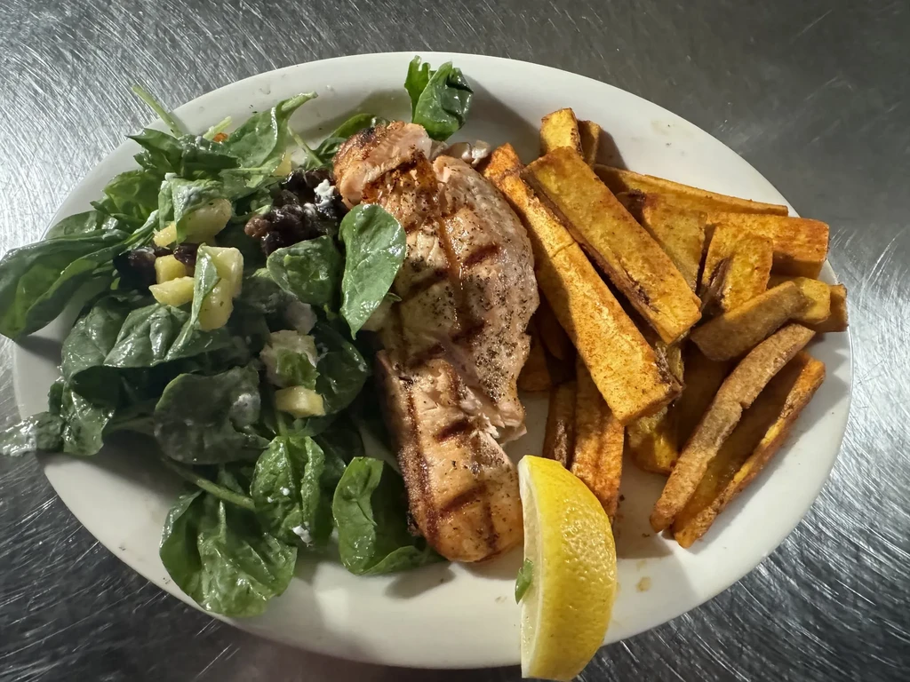 Grilled salmon, spinach salad, fries, and lemon wedge on a plate.