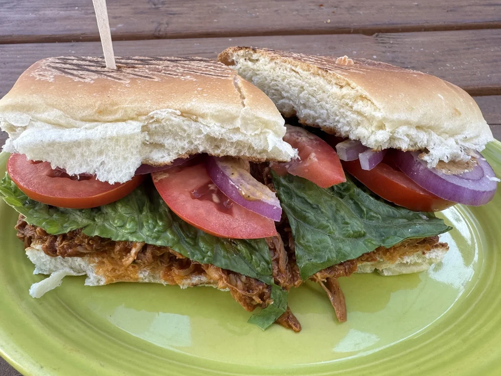A panini with pulled pork, lettuce, tomato, and red onion.