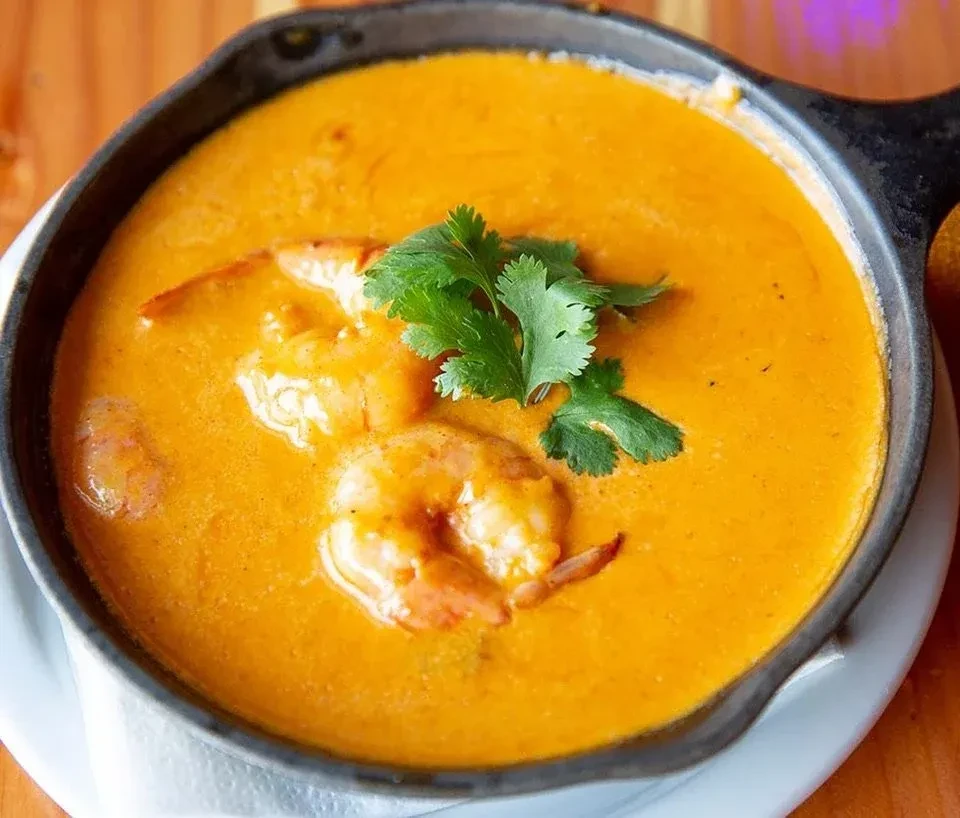 Shrimp in a skillet with a creamy orange sauce and cilantro.