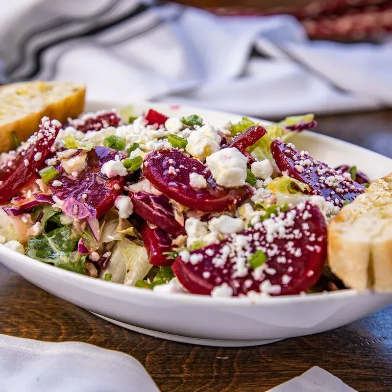 A white bowl of beet salad with feta, greens, and baguette slices.