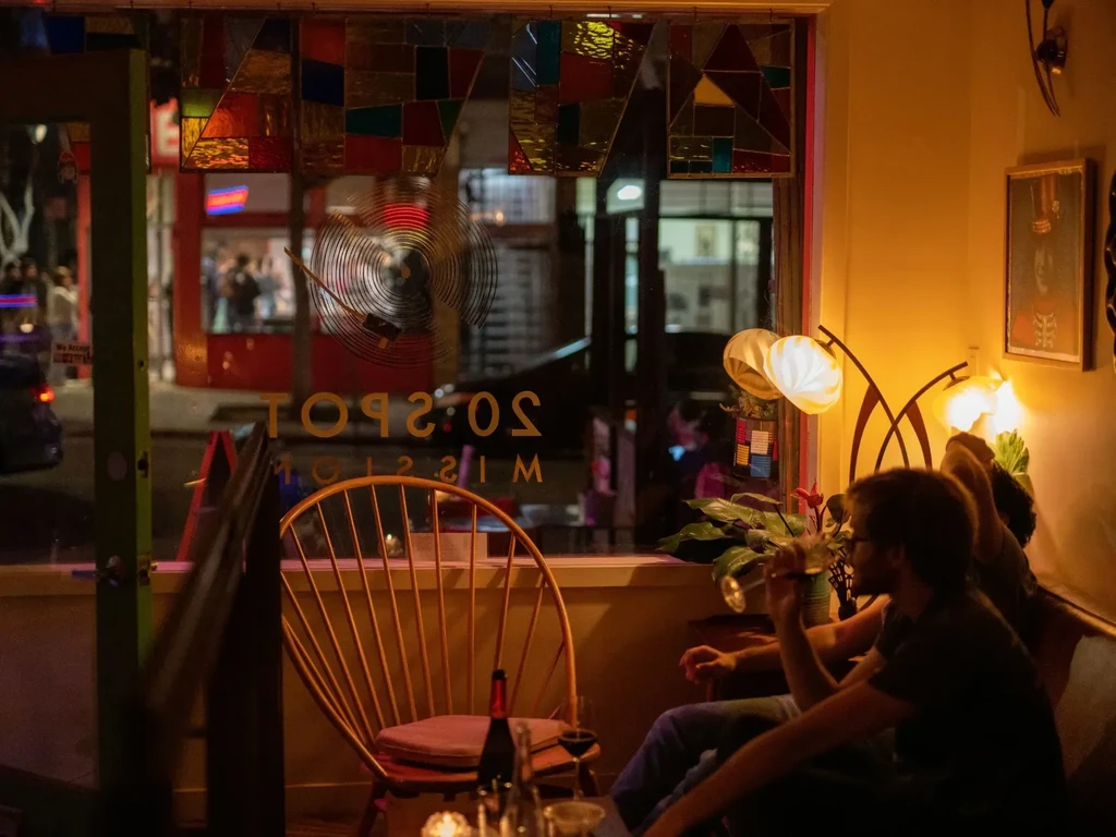 A man drinks wine in a warmly lit bar at night.